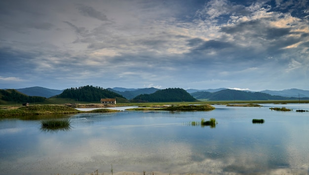 Maison solitaire au bord du lac dans les montagnes au coucher du soleil. Altaï