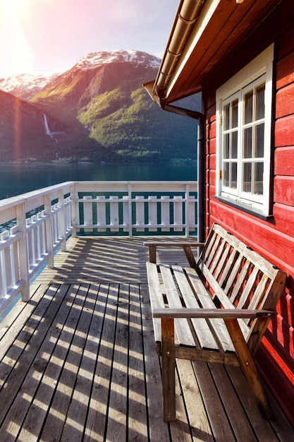 Photo maison traditionnelle norvégienne en bois rouge pour se tenir au bord du lac près du phare et des montagnes au loin, norvège