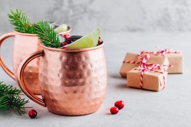 Maison de vacances Moscow Mule cocktail glacé dans une tasse en cuivre avec canneberges citron vert et romarin sur fond de pierre grise