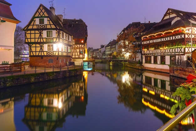 Maisons à colombages alsaciennes traditionnelles avec reflets miroir dans la Petite France pendant l'heure bleue du crépuscule décorée et illuminée à l'époque de Noël, Strasbourg, Alsace, France