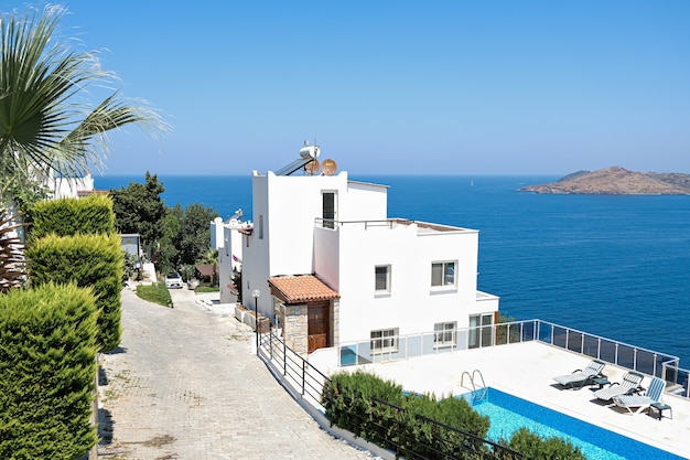 Maisons de villas de vacances blanches sur station avec vue mer et piscine et palmiers.