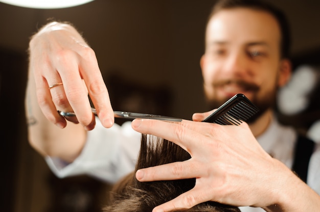 Maître coupe les cheveux et la barbe des hommes dans le salon de coiffure