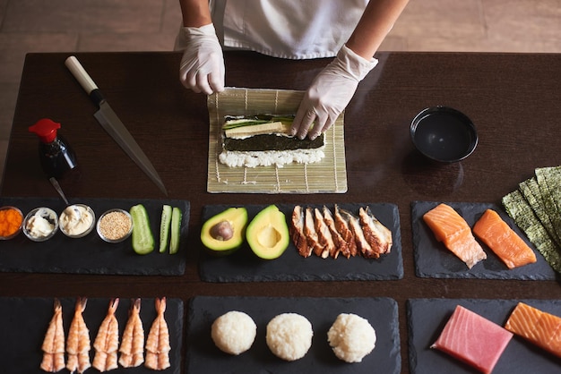 Maître faisant un rouleau de sushi avec du nori, du riz, du concombre et de l'omelette à l'aide d'un tapis de bambou. Vue rapprochée du processus. Vue depuis le sommet