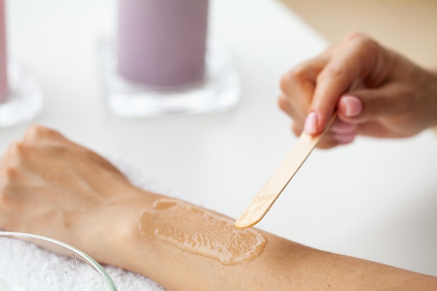 Le maître fait l'épilation des mains avec de la cire chaude en pâte de sucre dans un salon de beauté