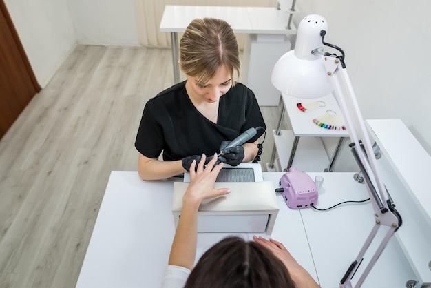 Le maître fait une manucure à une fille dans un salon de beauté à l'aide d'un routeur