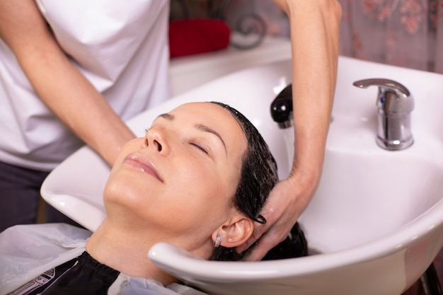 Le maître lave la tête du client dans le salon de coiffure, le coiffeur fait la coiffure pour une jeune femme.