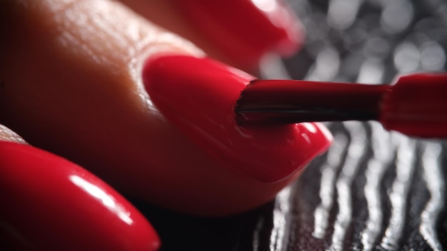 Le maître manucure applique un vernis rouge vif décoratif sur la plaque à ongles avec une brosse