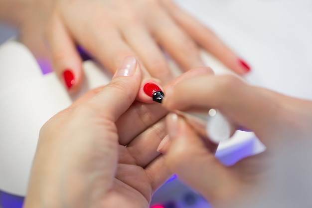 Le maître de manucure fait une manucure rouge sur la main de la jeune femme. Maître des ongles femme faisant des ongles à une cliente dans un salon de beauté. Prendre soin des mains