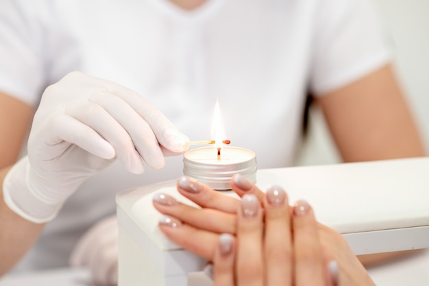 Maître de manucure en gants blancs allumant une bougie avec un match dans un salon de manucure