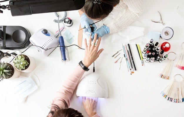 Maître de manucure en masque et gants mettant du vernis gel sur les ongles d'un client