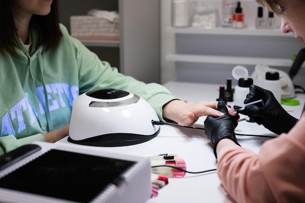 Maître manucure travaillant avec une cliente dans un salon de beauté Séchage des ongles dans une lampe ultraviolette