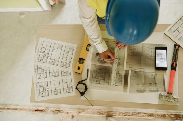 Photo maître d'œuvre ou architecte travaillant sur des plans de téléphone portable sur un chantier d'amélioration de l'habitat