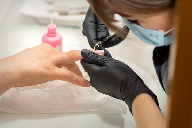 Maître des ongles enlevant la cuticule des ongles avec une pince, hygiène de manucure dans un salon de beauté.