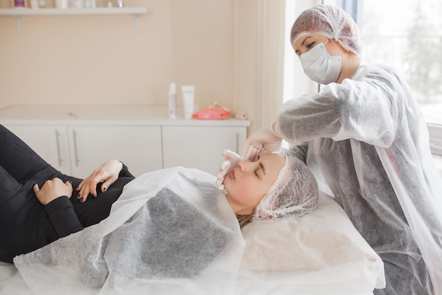 Maître réalisant une intervention esthétique pour son client. traitement de soins de la peau. femme faisant une procédure de soins du visage.