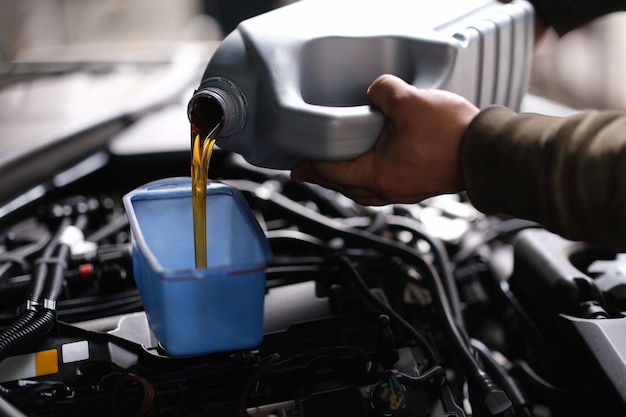 Maître réparateur versant de l'huile moteur dans un moteur de voiture en gros plan