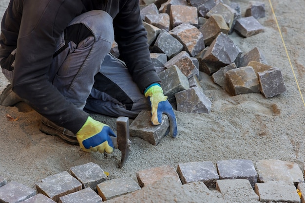 Le maître de route en gants pose des pavés en couches route de pierre par un travailleur professionnel à l'aide de pierres et de marteau