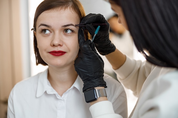 Maître des sourcils professionnel fait son travail pour une belle femme au salon de beauté