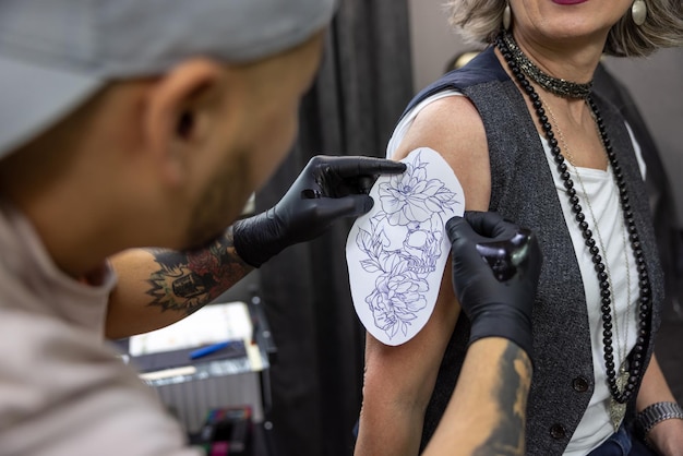 Maître de tatouage appliquant un croquis de tatouage sur l'épaule de la femme