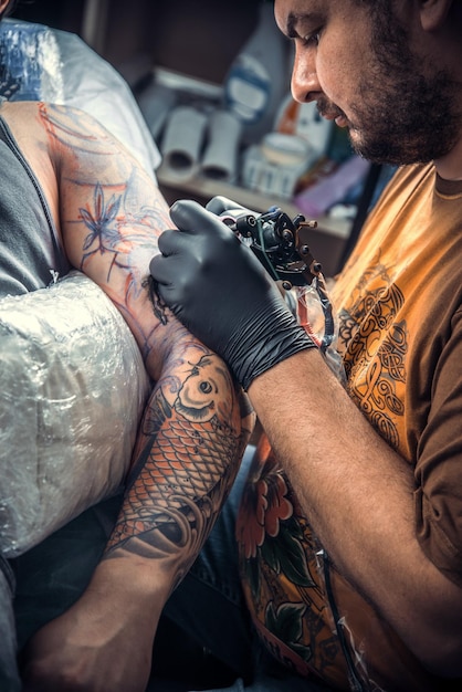 Maître de tatouage au travail dans un salon de tatouage./Tatoueur professionnel travaillant dans un studio de tatouage.