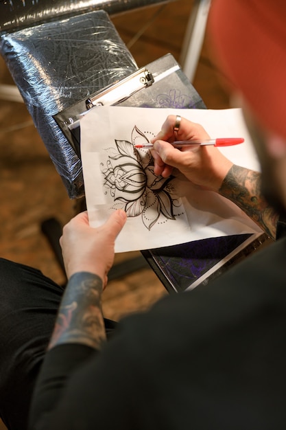 Le maître de tatouage caucasien barbu professionnel travaille dans un studio atmosphérique confortable