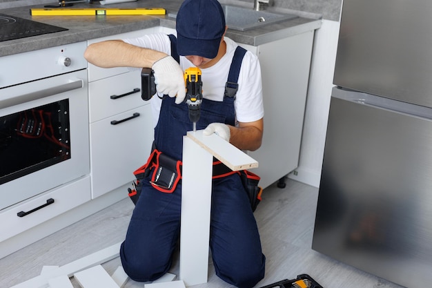 Photo le maître en uniforme assemble de nouveaux meubles dans la cuisine avec un tournevis