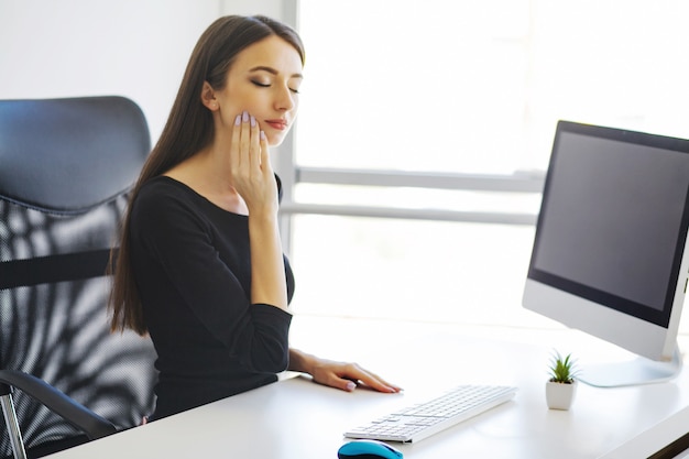 Mal de dents. Concept de santé dentaire. Portrait de jeune femme triste, ayant mal aux dents, assise dans son bureau.