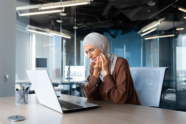 Mal de dents sur le lieu de travail une jeune femme travaillant au bureau à une table derrière un ordinateur portable la tient