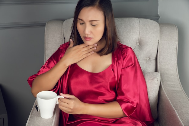 Un mal de gorge est une douleur, des égratignures ou une irritation, les femmes asiatiques en vêtements de nuit en soie rouge avec reflux acide la nuit