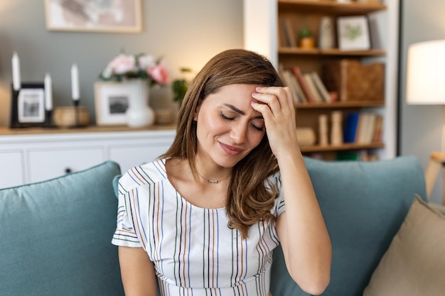 Mal de tête Photo en gros plan d'une jeune femme assise sur un canapé qui se touche la tête alors qu'elle souffre d'une migraine