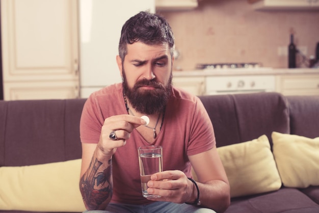 Un malade barbu jette une pilule de grippe dans un verre d'eau