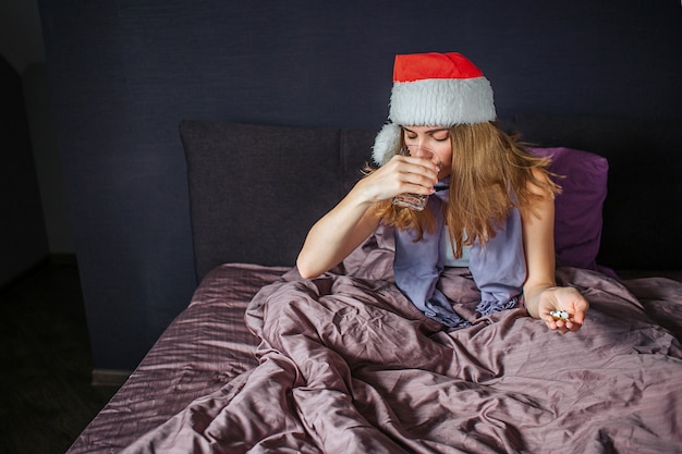 Malade jeune femme au chapeau rouge de Noël est assise sur le lit