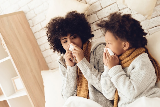 Malade mère africaine et sa fille reniflant assis sur le lit.