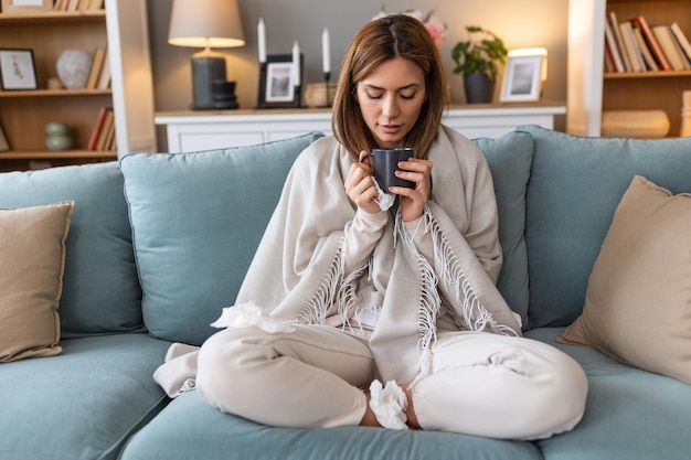 Photo maladie concept de problème de virus saisonnier femme malade ayant la grippe buvant du thé sur le canapé femme malade allongée au lit avec une fièvre élevée grippe froide et migraine