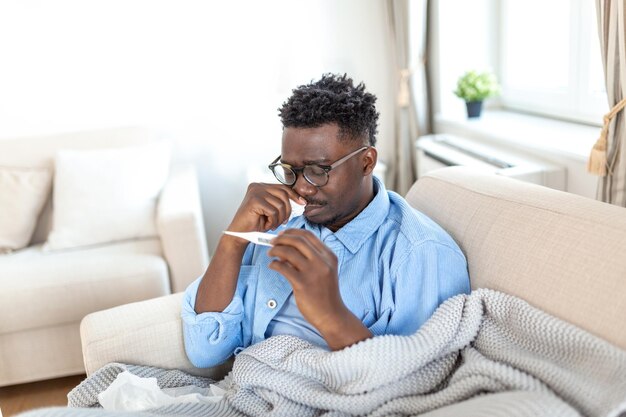 Photo maladie concept de problème de virus saisonnier homme malade ayant la grippe allongé sur le lit en regardant la température sur le thermomètre homme malade allongé au lit avec une fièvre élevée gripe froide coronavirus covid-19