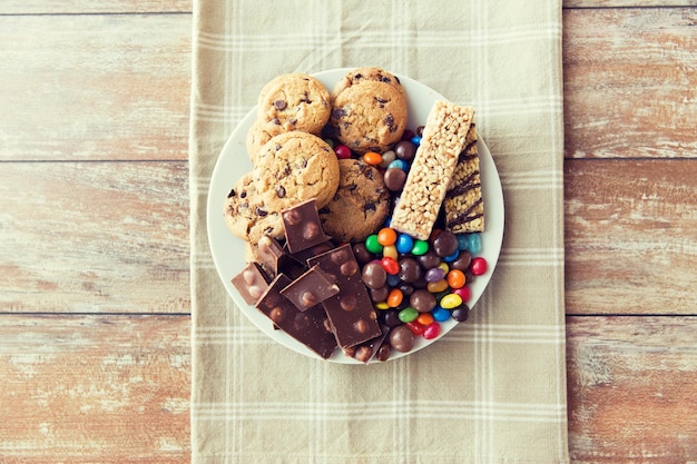 malbouffe, bonbons et concept de mauvaise alimentation - gros plan de bonbons, chocolat, muesli et biscuits sur assiette