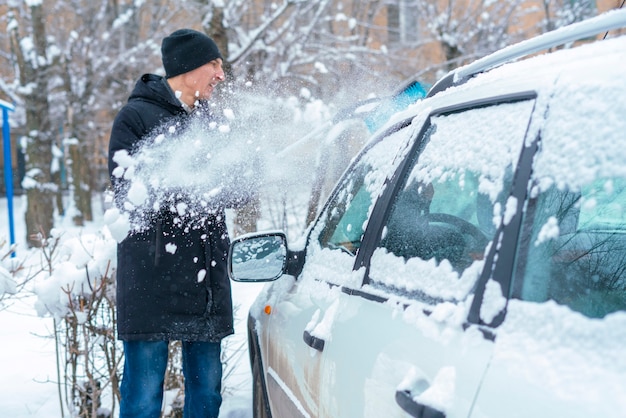 Mâle adulte enlevant la neige du toit de la voiture avec une brosse en hiver