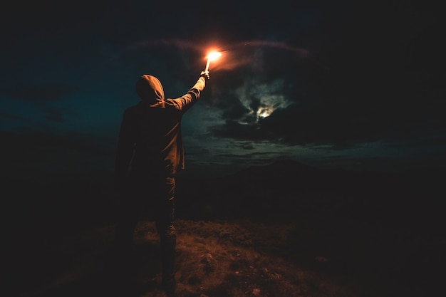 Le mâle avec un bâton lumineux de feu d'artifice se tenant sur la montagne de nuit