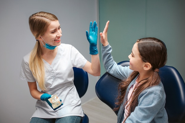 Mâle dentiste donnant cinq haut pour fille dans un fauteuil dentaire