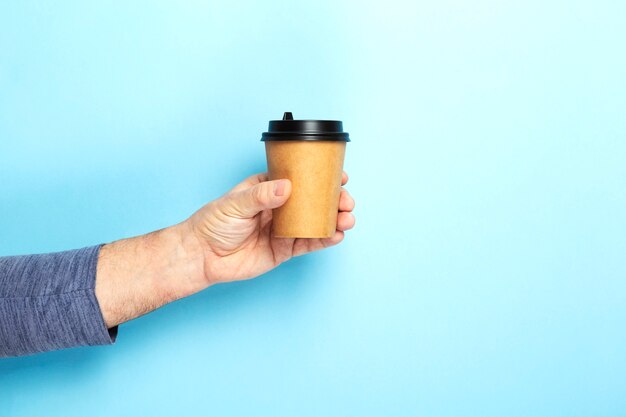 Mâle détient la tasse de papier à la main avec du café sur fond bleu