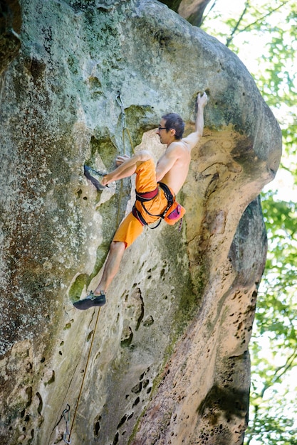 Mâle grimpeur escalade avec une corde sur un mur rocheux