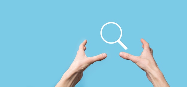 Mâle main tenant loupe, icône de recherche sur fond bleu. Optimisation des moteurs de recherche de concept, support client. Navigation sur les informations de données Internet. Concept de mise en réseau.