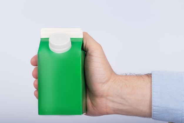 Mâle main tenant un paquet vert pour le lait ou le jus sur fond blanc. Copiez l'espace, mock up