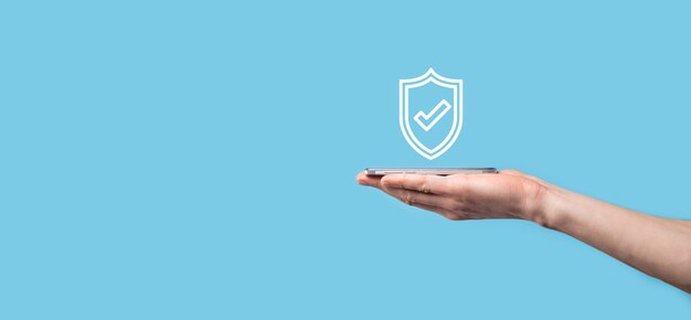 Photo mâle main tenant protéger le bouclier avec une icône de coche sur fond bleu. ordinateur de sécurité de réseau de protection et sécurise votre concept de données.
