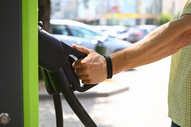 Mâle main tenir le pistolet un fond de station de ville de charge électrique