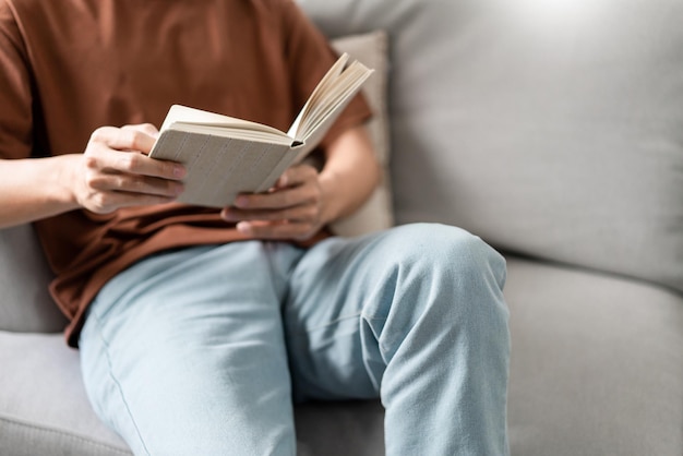 Le mâle avec ses lunettes assis sur le canapé gris s'y adossant et lisant un livre