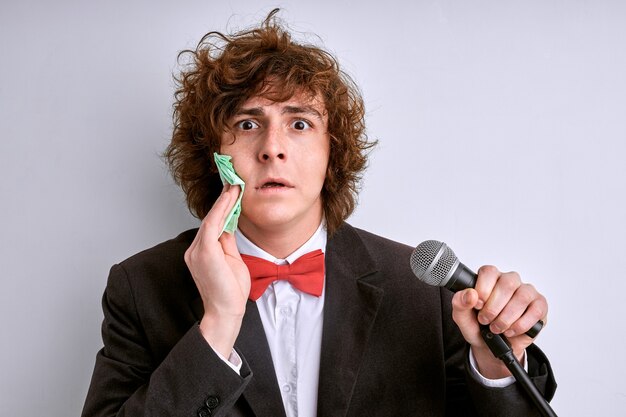 Le Mâle En Sueur A Peur D'une Mauvaise Présentation. Homme Stressé Avec Microphone, Orateur Public En Costume Isolé Sur Fond Blanc. Mec Bouclé A Peur De Prononcer Un Discours Devant Une Foule De Personnes Ou Un Public