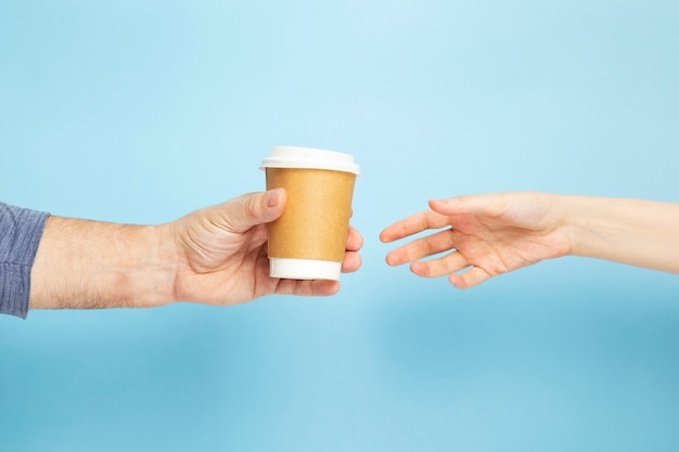 Mâle tient la tasse de papier à la main avec du café femelle prend la tasse sur fond bleu