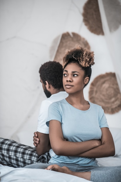 Malentendu. Triste jeune femme américaine adulte avec ses bras croisés sur la poitrine assis avec le dos au mari