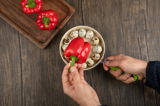 Mâles mains tenant pan d'oeufs de caille et poivrons rouges sur la surface en bois