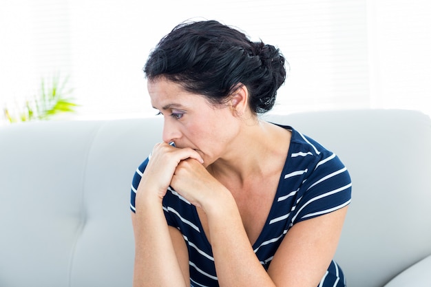 Malheureuse femme assise sur le canapé sur fond blanc